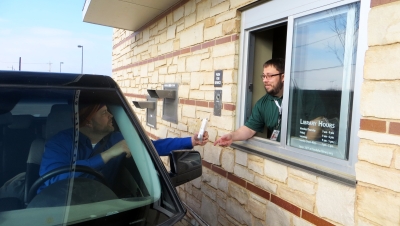 Library staff member handing a patron an item through the library's drive up service window