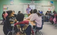 Classroom full of students and desks with teacher at the front of the room