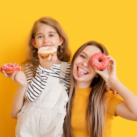 photo of a mother and daughter acting silly eating frosted donuts on a yellow background