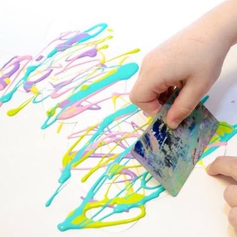 child using a paint scraper to spread multicolored pastel paint