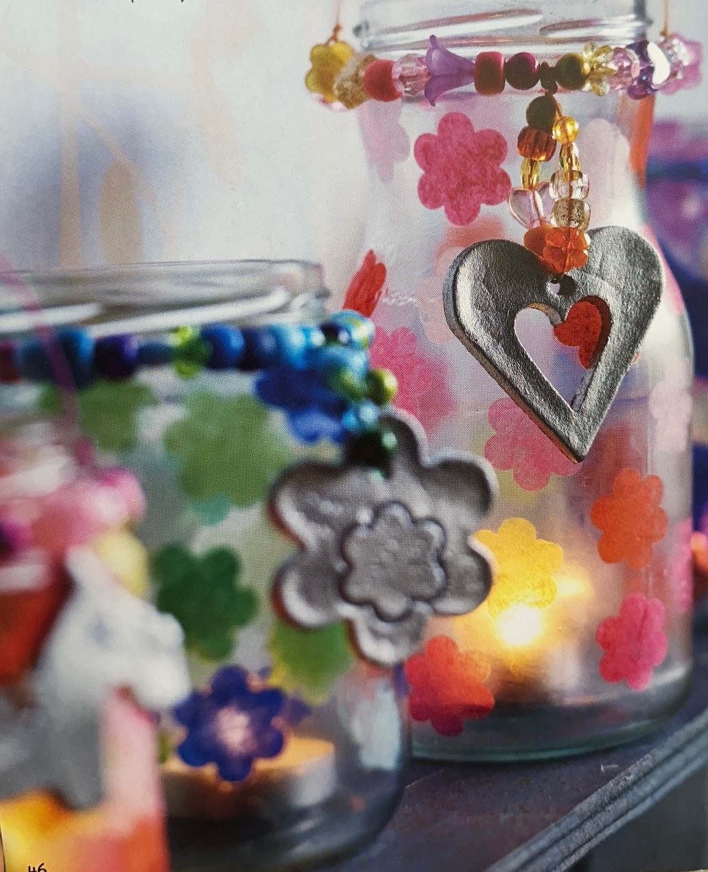 beads and tissue paper flowers decorating a jar with a candle in it