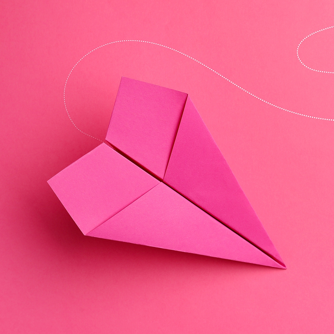 photo of a pink paper airplane on a pink background