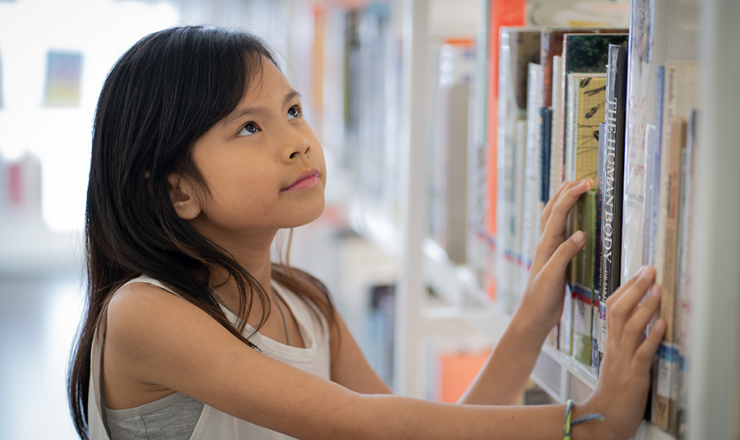 Young girl looking at books on the library book shelf