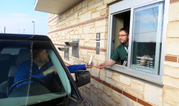 Library staff member handing a patron an item through the library's drive up service window