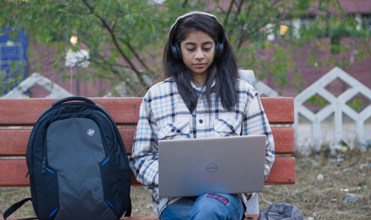 girl sitting on bench using computer and listening to headphone